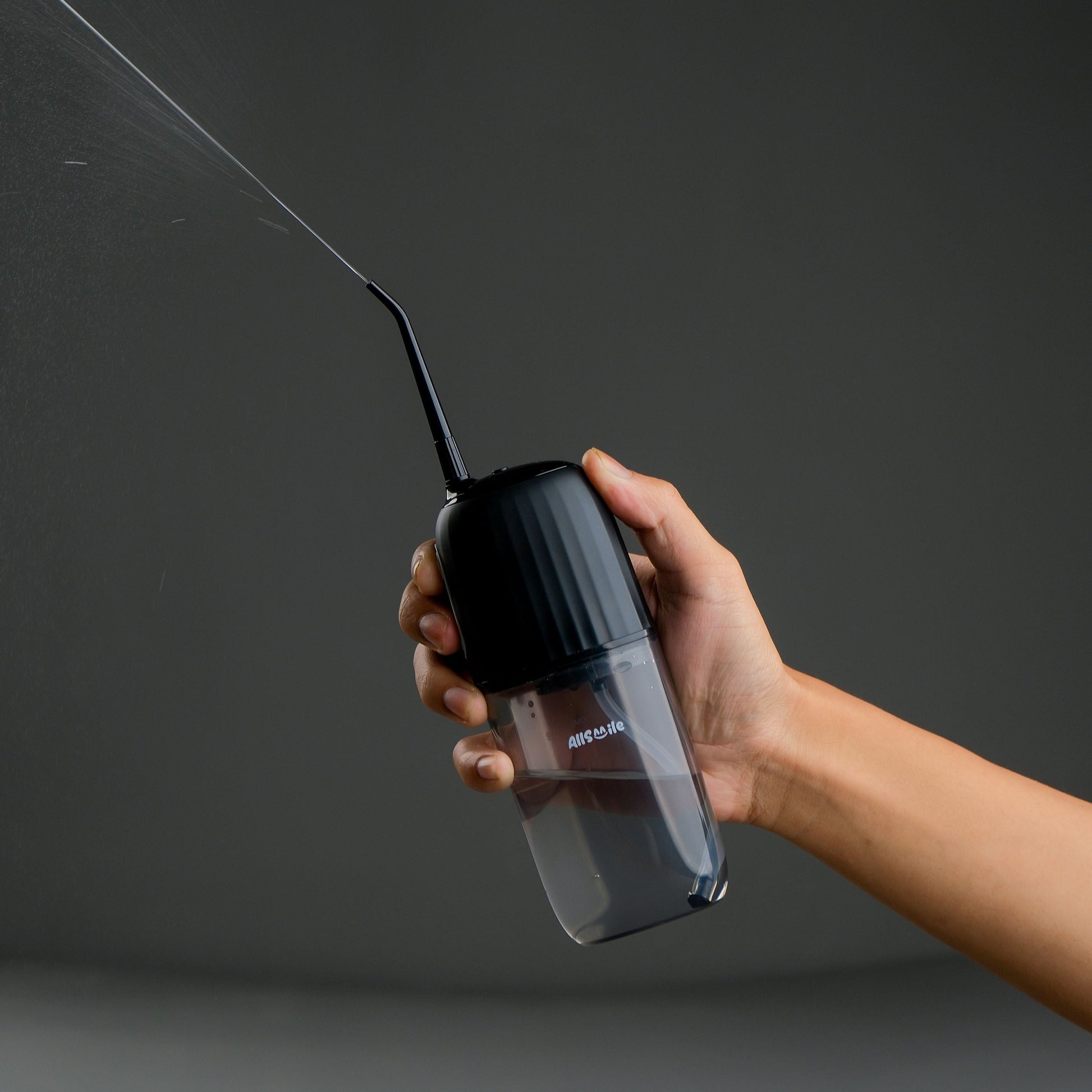 A hand holding a portable water flosser with water flowing out of its spout. "घरमै दाँत सफा गर्ने device."